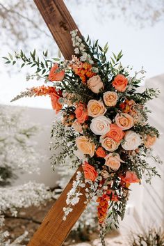 an orange and white floral arrangement hanging from a wooden cross at a wedding ceremony in the desert