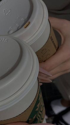 two coffee cups are stacked on top of each other with their lids down and one cup is being held by someone's hand