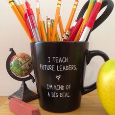 a black coffee cup filled with pencils next to an apple