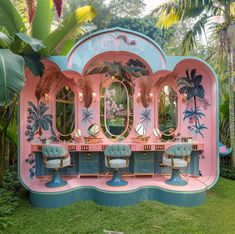 a pink and blue vanity with mirrors on it in the middle of some grass next to palm trees