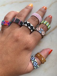 a woman's hand with five different colored rings on her fingers and one is wearing an orange nail polish