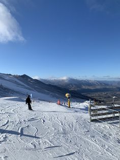 a person standing on top of a snow covered slope next to a fence and mountains