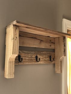 a wooden shelf with two hooks on the top and an open door in the background