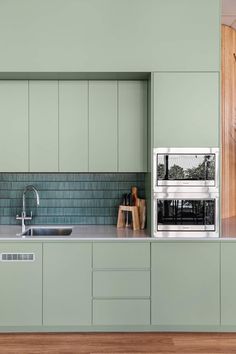 a kitchen with green cabinets and a stainless steel microwave on the wall above the sink