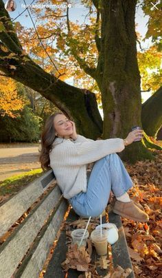 a woman sitting on a park bench with her arms outstretched and holding a cup of coffee