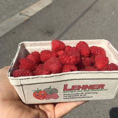 a person holding a box of raspberries in their left hand and the other hand