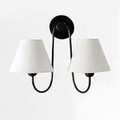 two white lamps hanging from a black metal wall light with three shades on each lamp