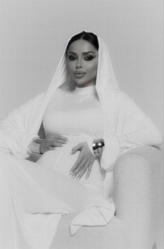 a black and white photo of a woman sitting on a chair with a veil over her head