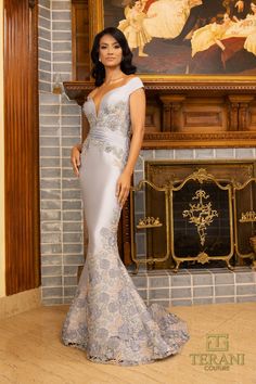 a woman standing in front of a fireplace wearing a white and blue dress with flowers on it