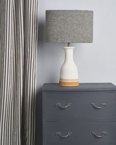 a white and grey dresser with a lamp on it next to a striped drapes