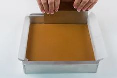 a person with their hands on top of a metal pan filled with brown liquid,