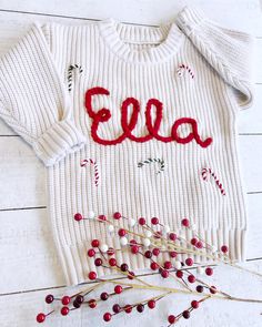 a white sweater with the word ella on it next to some red berries and twigs