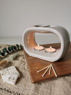 two candles sitting on top of a wooden table next to a white vase and other items