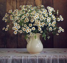 a vase filled with white and yellow daisies on top of a cloth covered table