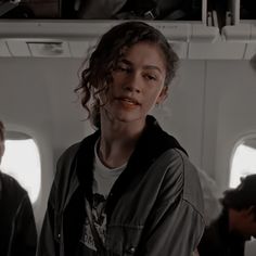 a woman standing in an airplane looking at the camera with two other people behind her