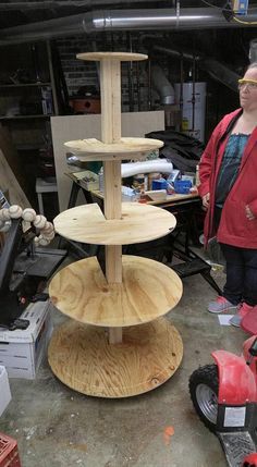 a woman standing next to a three tiered wooden stand in a garage with tools on the floor