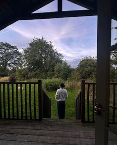 a person standing on a porch looking out at the grass and trees in the distance