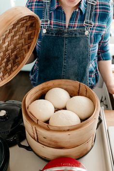 a woman standing in front of a wooden basket filled with dumplings on top of a kitchen counter