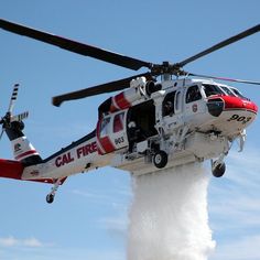 a red and white helicopter flying through the air with water pouring out of it's sides