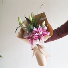 a person is holding a bouquet of flowers in their left hand and the other hand has a brown paper bag on it