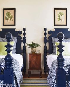 two twin beds with blue headboards and green pillows in a white walled bedroom area