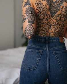 a woman with tattoos on her back standing in front of a bed