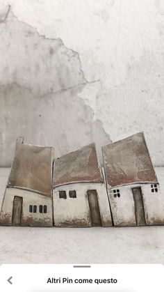 three small white houses sitting next to each other on top of a table in front of a wall