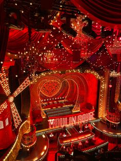 the interior of a theater with red lights and decorations on the walls, seats and chandeliers