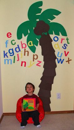 a child sitting on the floor in front of a wall with letters and a palm tree