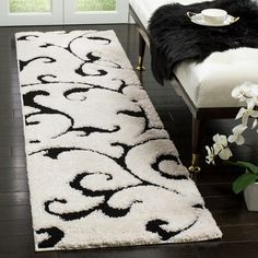 a black and white rug on a wooden floor next to a bench with flowers in it