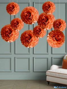 five orange flowers hanging from strings in front of a blue wall and white couches