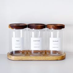 three glass jars with labels on them sitting on a wooden tray