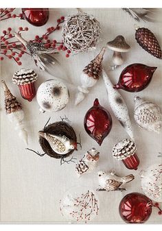 christmas ornaments are arranged on a white tablecloth with red berries, pine cones and acorns