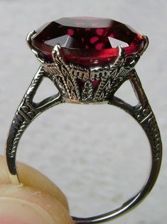 This is an Edwardian reproduction filigree ring in antiqued solid sterling silver. The round full cut high quality Simulated Red Ruby solitaire gemstone is 12mm in diameter. The inside of the band is marked 925 for sterling silver. Victorian Style Ruby Ring With Center Stone, Antique Red Rings With Prong Setting, Antique Red Ring With Prong Setting, Antique Ruby Ring With Intricate Design For Gift, Antique Ruby Ring With Intricate Design As Gift, Antique Red Ruby Ring With Round Cut, Antique Ruby Ring With Round Cut, Wedding Ruby Ring With Intricate Design, Ornate Round Filigree Ring Collectible