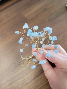 a hand holding a wire and blue glass beaded hair piece on top of a wooden table