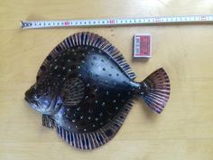 a metal fish sitting on top of a wooden table next to a ruler and pencil