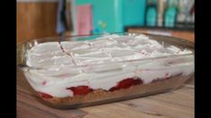 a dessert dish with white icing and strawberries in it on a wooden table