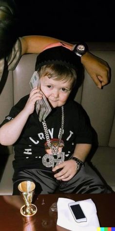 a young boy sitting in a chair talking on a cell phone while holding a cup