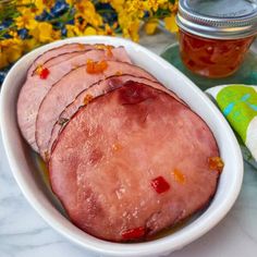 sliced ham in a white bowl next to a jar of honey and napkins on a marble table