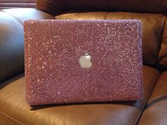 an apple laptop covered in pink sequins sitting on a brown leather couch next to a window