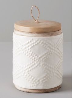 a white canister with a wooden lid and ring on the top that is hanging from a rope