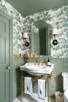 a bathroom with green and white wallpaper, gold faucet, sink and mirror