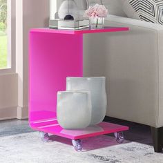 a white vase sitting on top of a pink shelf in front of a couch next to a window