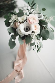 an arrangement of flowers in a vase on a table with pink ribbon and greenery