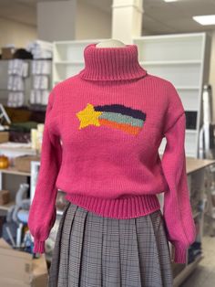 a woman's pink sweater with an arrow embroidered on the front, and plaid pleated skirt