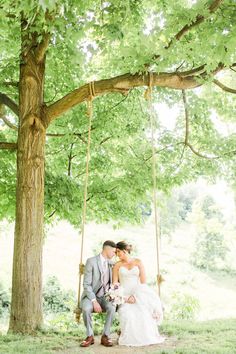 a bride and groom sitting on a swing under a tree