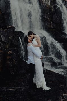 a bride and groom kissing in front of a waterfall