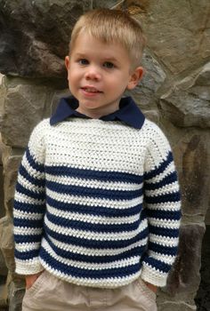 a young boy wearing a blue and white sweater standing in front of a rock wall