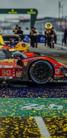 a red and yellow race car driving down a wet track with confetti on the ground