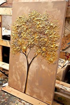 a painting with gold leaves on it in an art studio, next to some paintbrushes